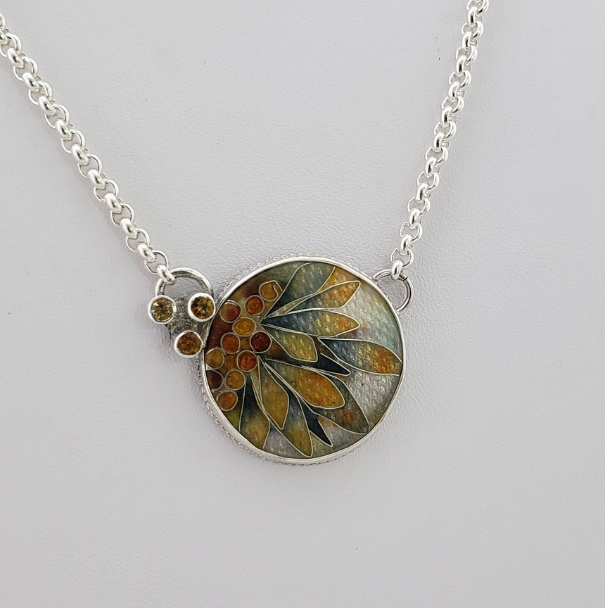 Cloisonne Enamel on a textured fine silver base.  Many layers of enamel from gold to deep greens and grays have been layered in this pendant.  Small Citrine stones are set off to one side.  A sterling chain is attached with a lobster clasp.