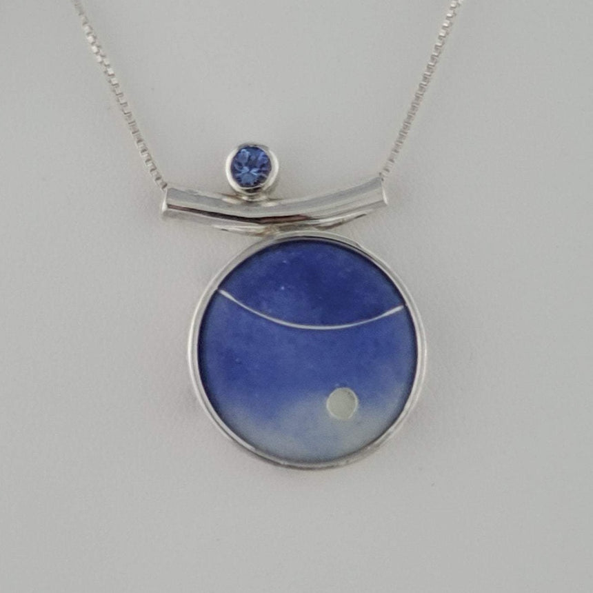 Twilight purple blue has a focal clear circle and a stripe of fine silver wire.  Accented with a 4 mm Tanzanite Stone to one side and a sterling silver box chain.